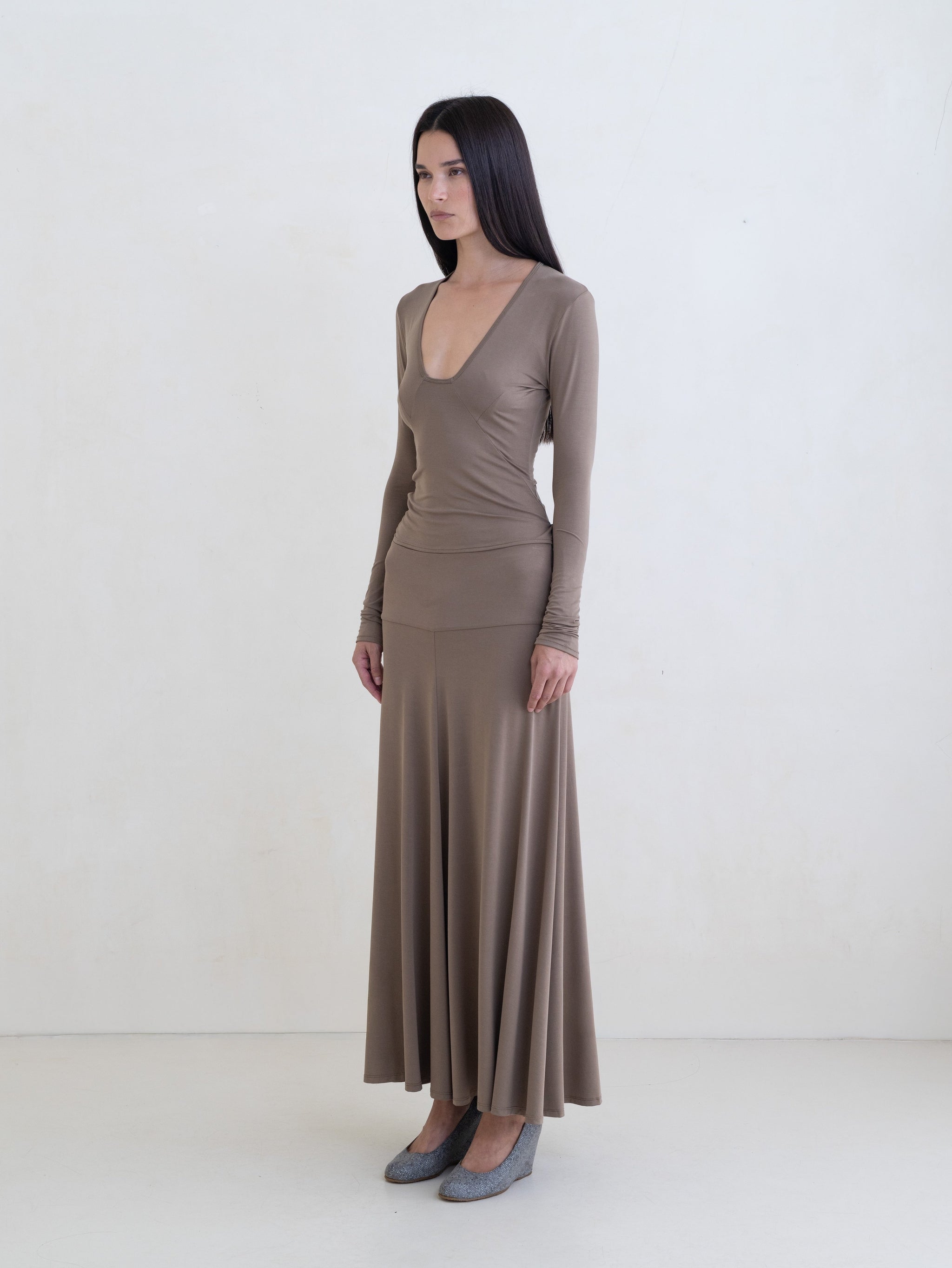 Woman wearing a taupe long sleeve top and a taupe maxi skirt on a white background.