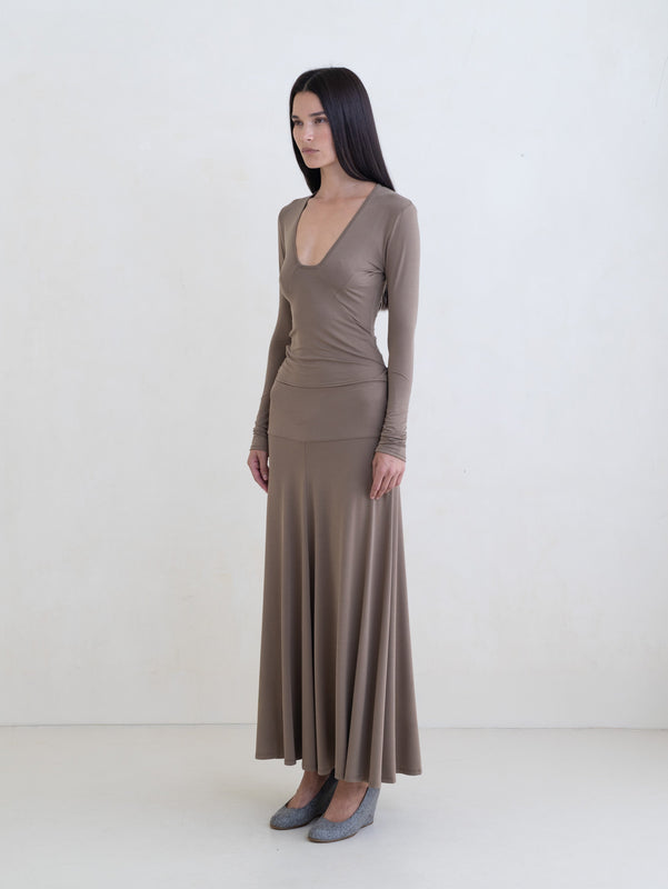 Woman wearing a taupe long sleeve top and a taupe maxi skirt on a white background.