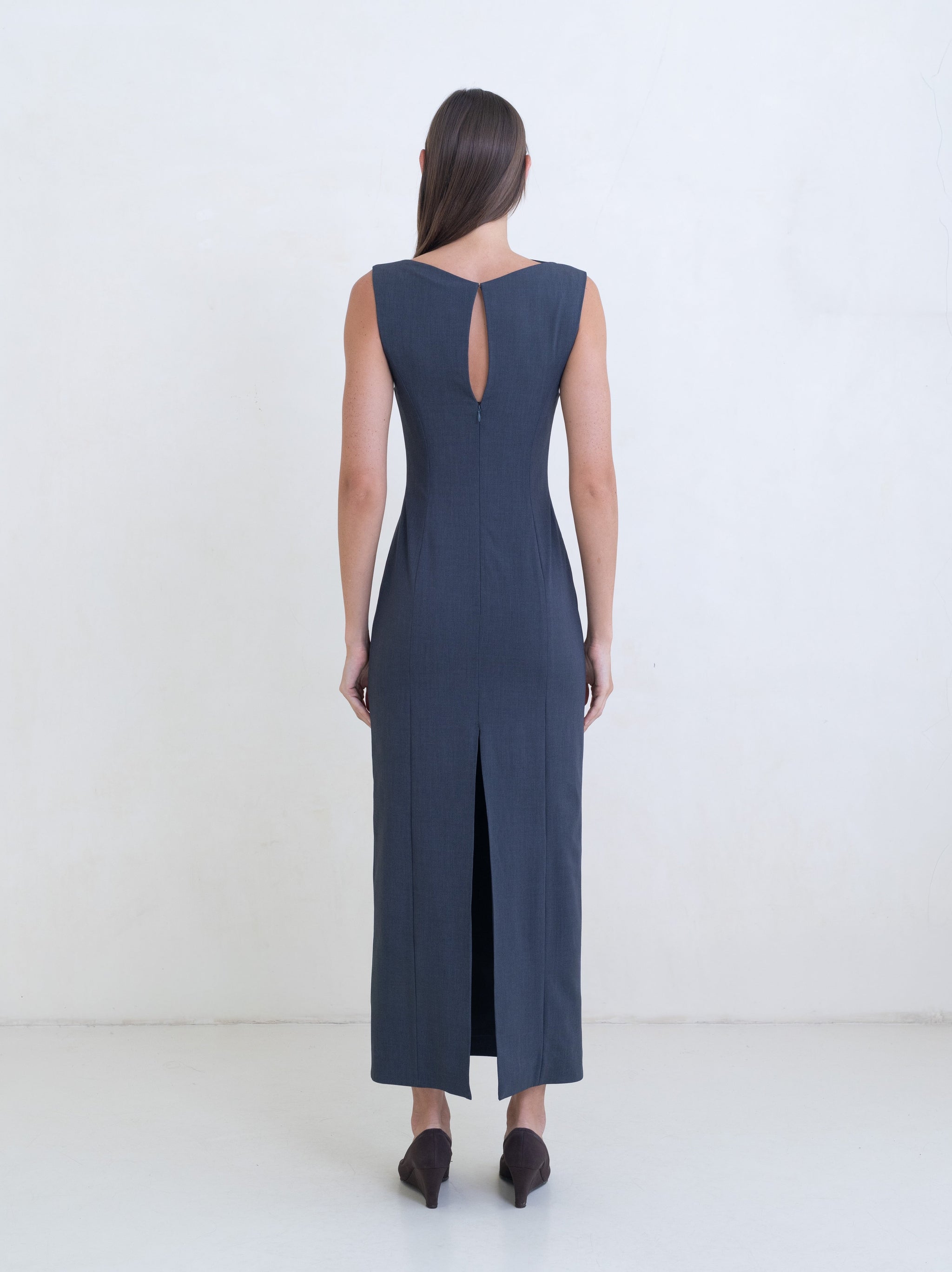 Woman wearing a dark gray sleeveless column dress on a white background. 