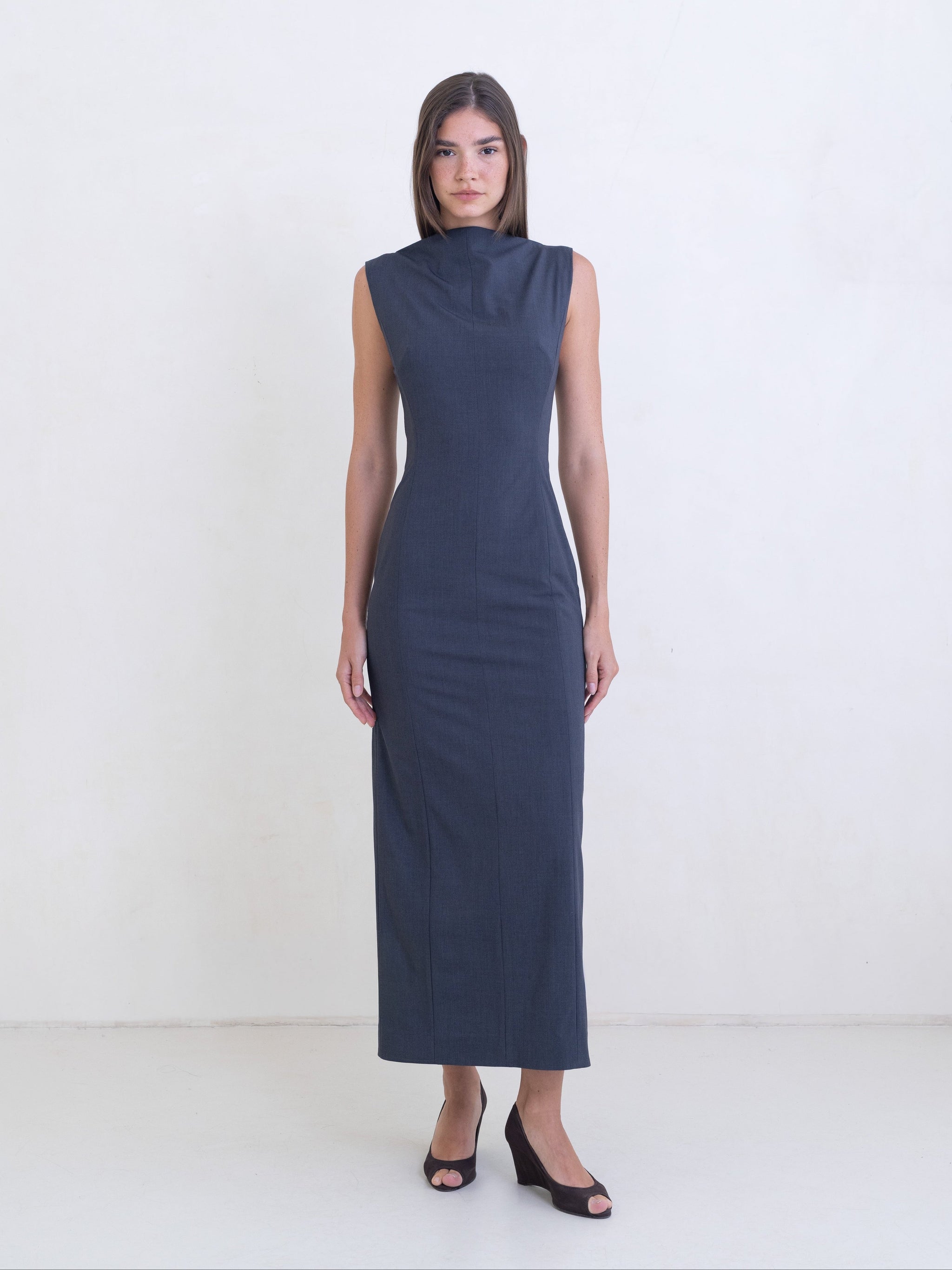Woman wearing a dark gray sleeveless column dress on a white background. 