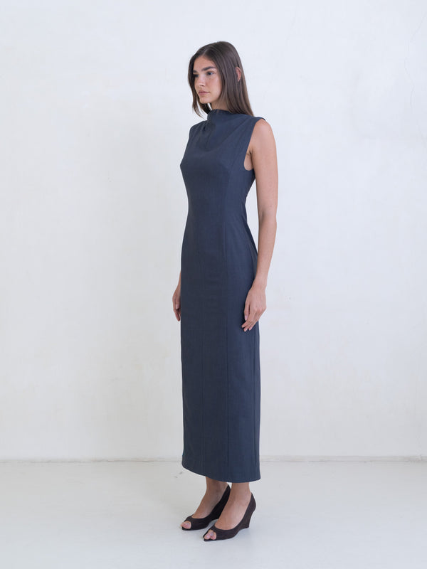 Woman wearing a dark gray sleeveless column dress on a white background. 