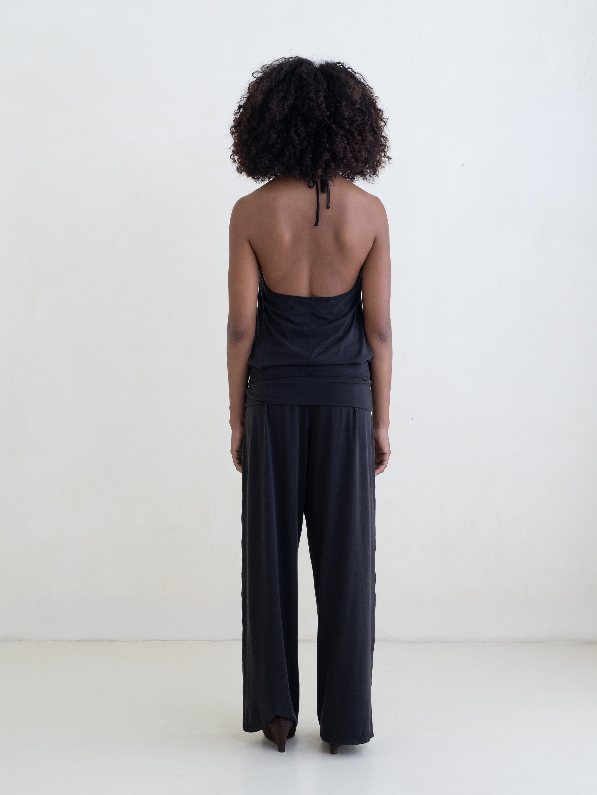 Woman wearing a black halter neck tank top and black straight leg pants on a white background. 
