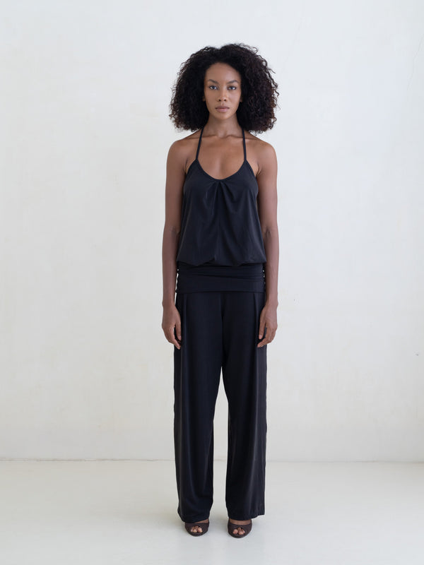 Woman wearing a black halter neck tank top and black straight leg pants on a white background. 