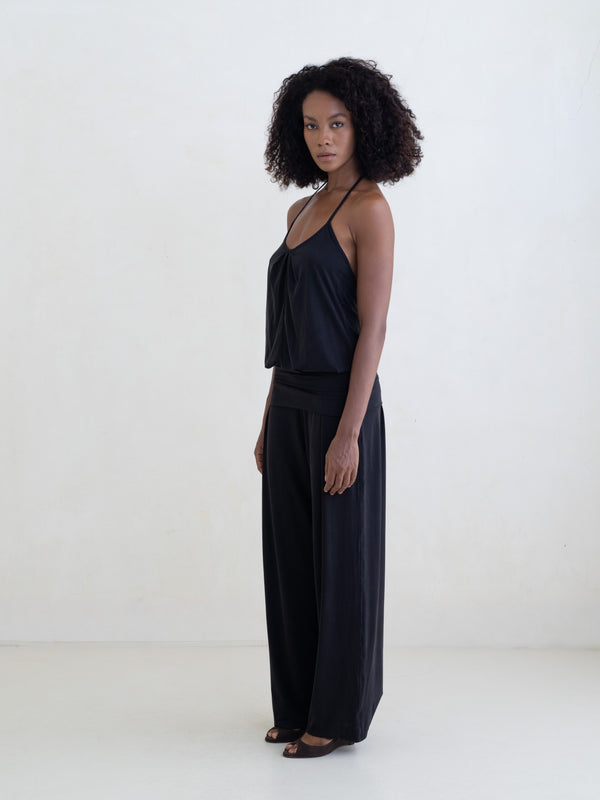 Woman wearing a black halter neck tank top and black straight leg pants on a white background. 