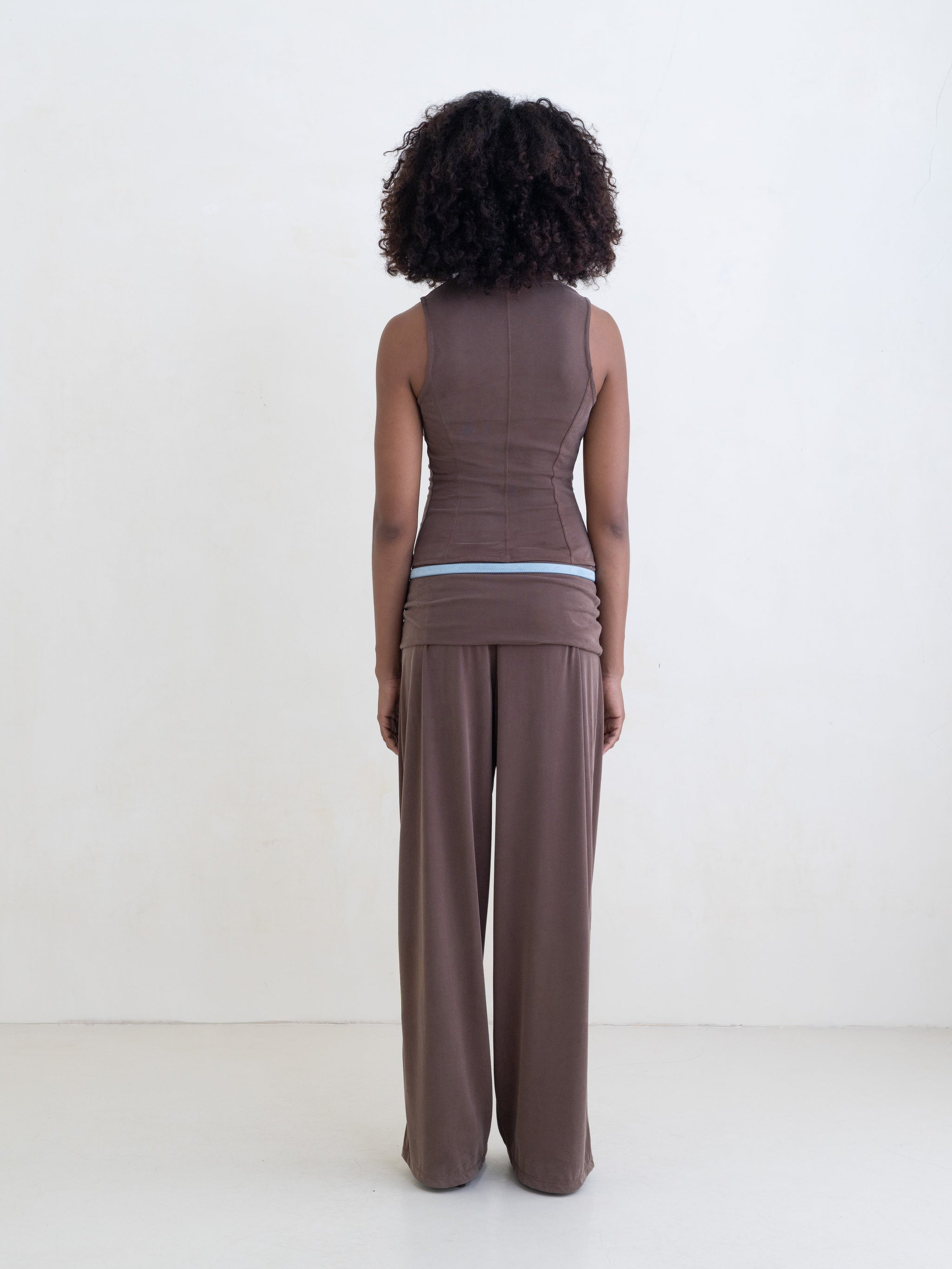 Woman wearing a brown sleeveless top and brown straight leg pants on a white background.