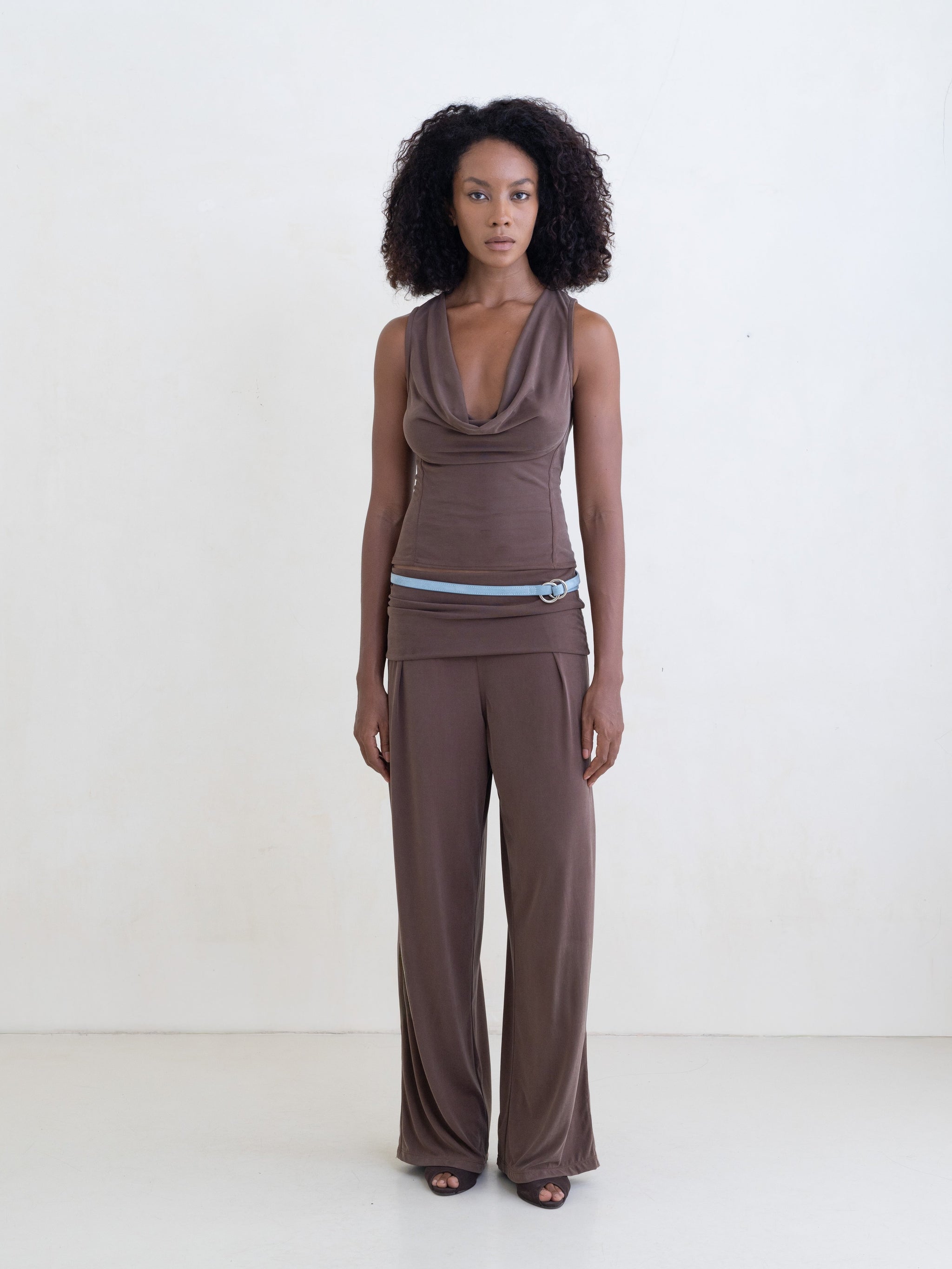 Woman wearing a brown sleeveless top and brown straight leg pants on a white background.