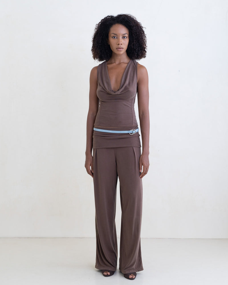 Woman wearing a brown sleeveless top and brown straight leg pants on a white background.