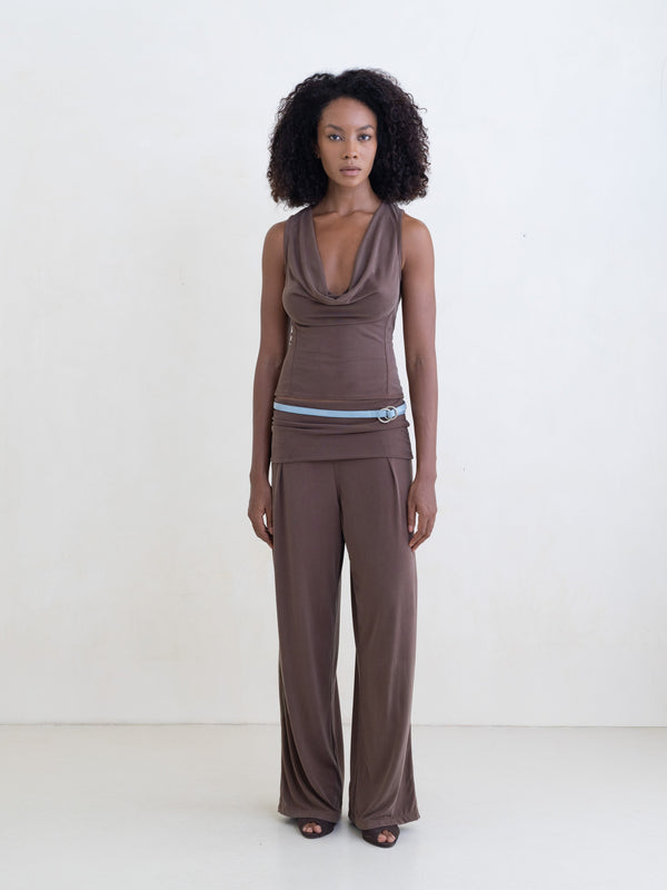 Woman wearing a brown sleeveless top and brown straight leg pants on a white background.