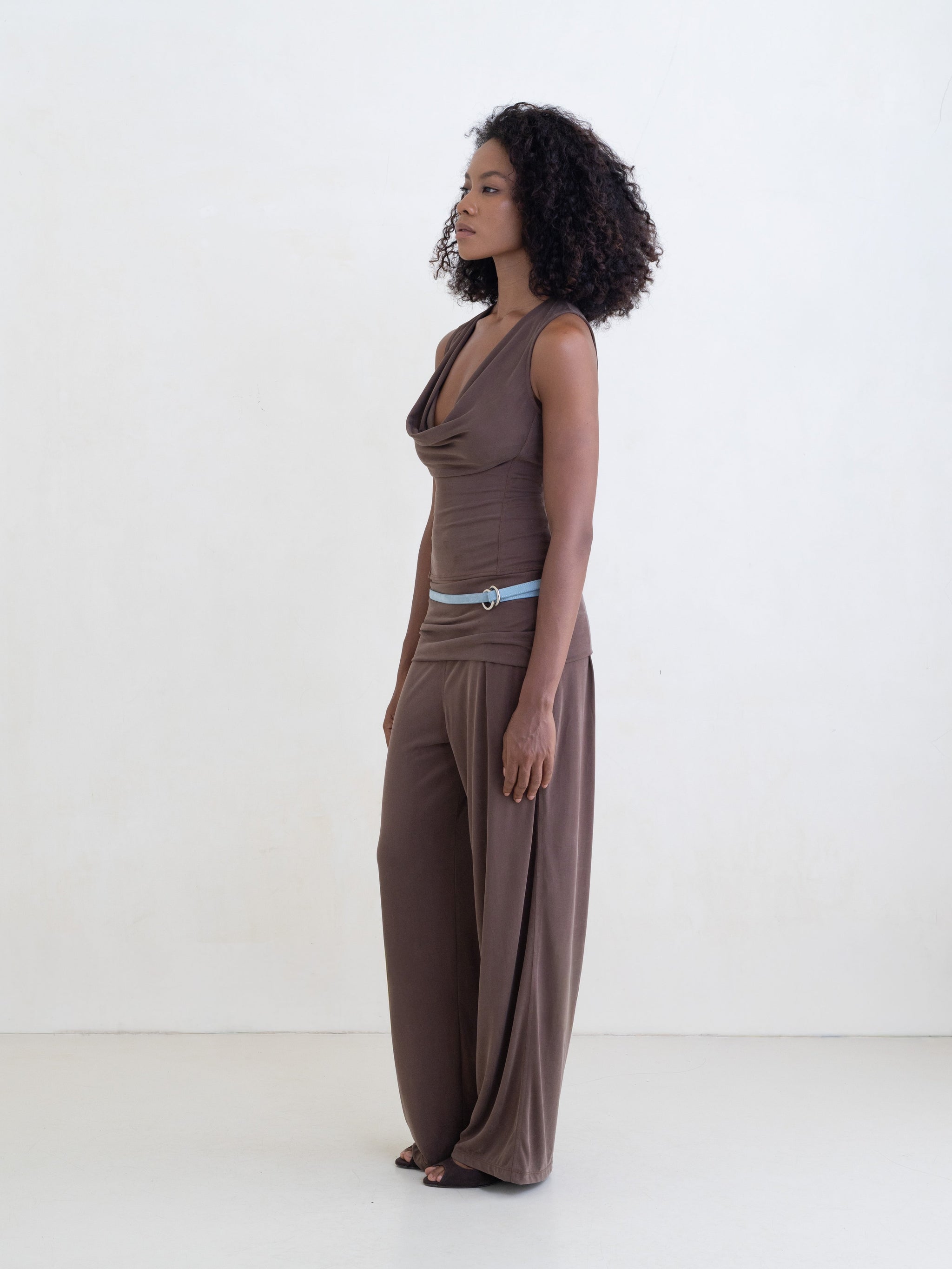 Woman wearing a brown sleeveless top and brown straight leg pants on a white background.