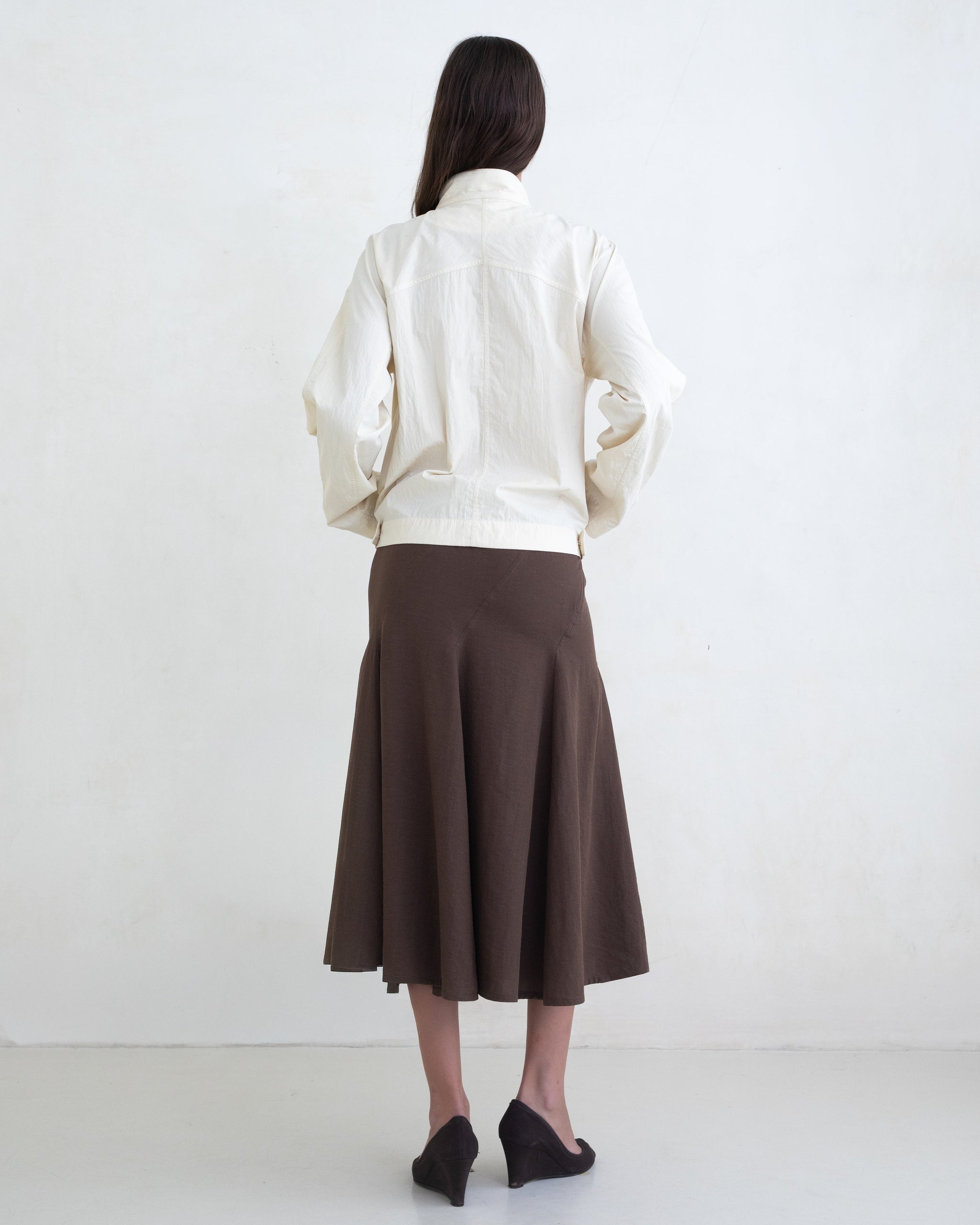 Woman wearing a cream jacket and a brown midi skirt on a white background. 