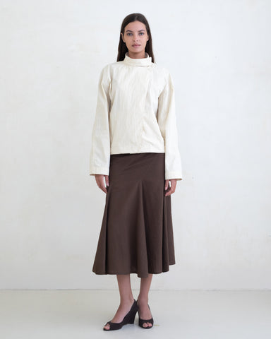 Woman wearing a cream jacket and a brown midi skirt on a white background. 