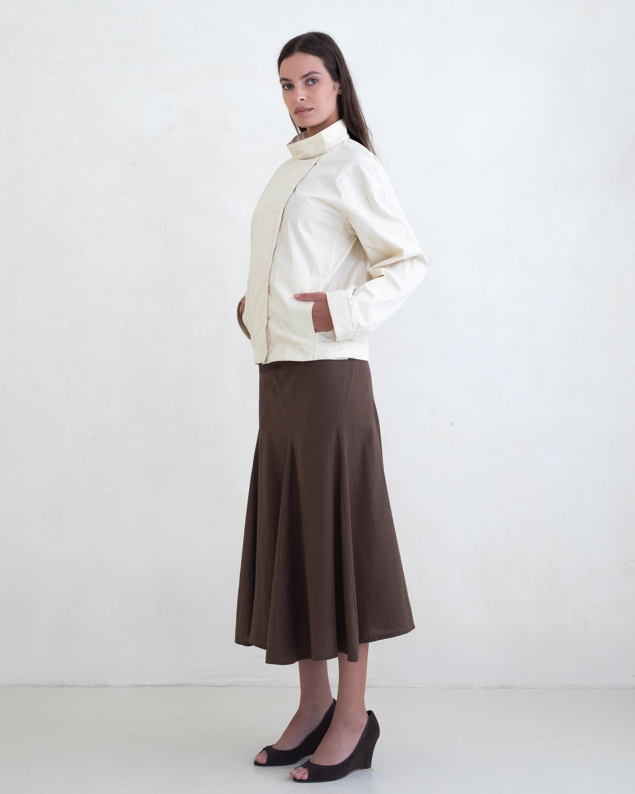 Woman wearing a cream jacket and a brown midi skirt on a white background. 