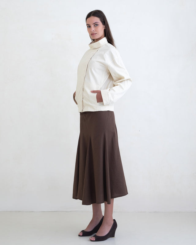 Woman wearing a cream jacket and a brown midi skirt on a white background. 