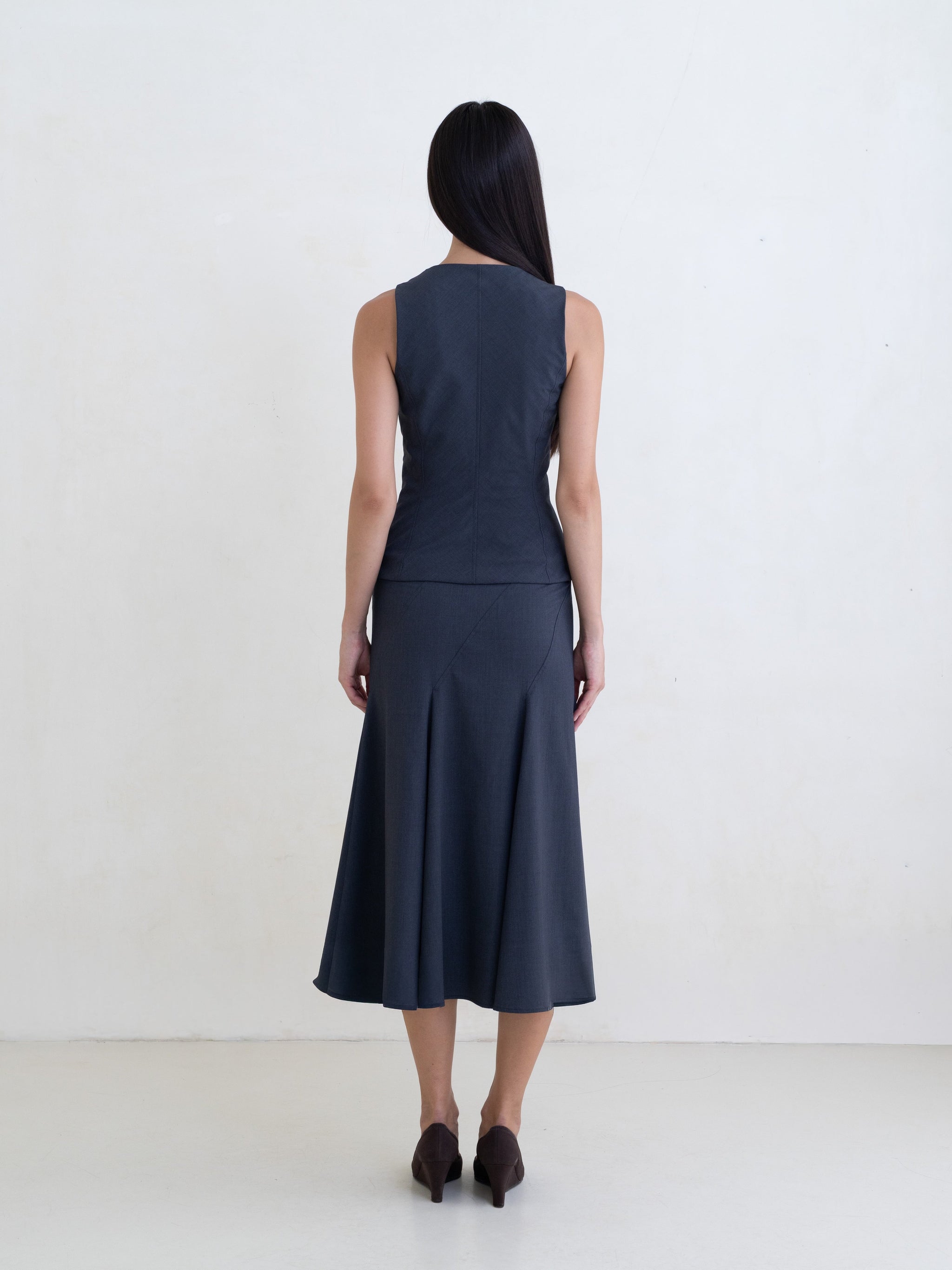 Woman wearing a dark gray sleeveless top and a dark gray flared midi skirt on a white background. 