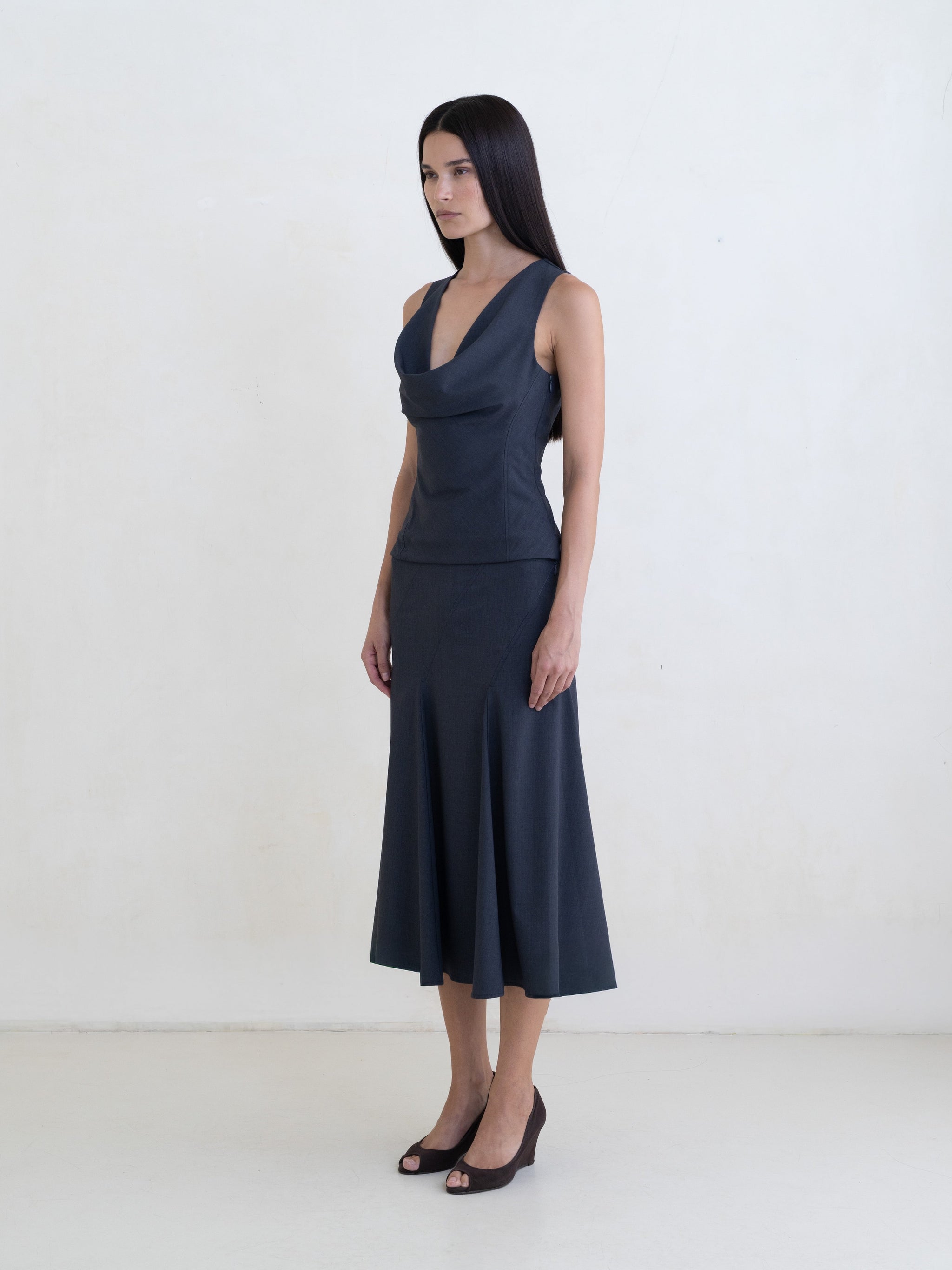 Woman wearing a dark gray sleeveless top and a dark gray flared midi skirt on a white background. 
