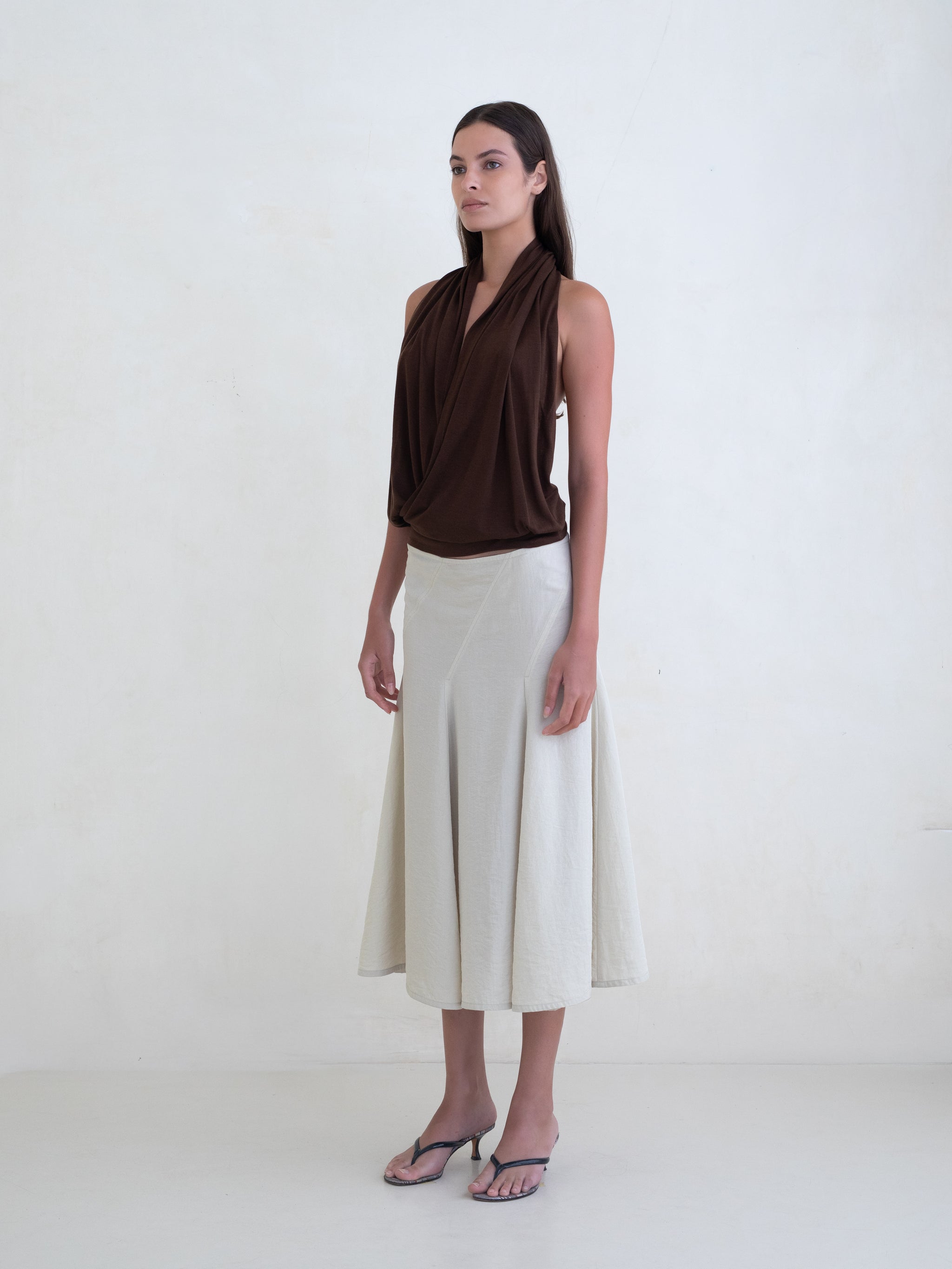 Woman wearing a brown draped halter top and a cream midi skirt on a white background.  
