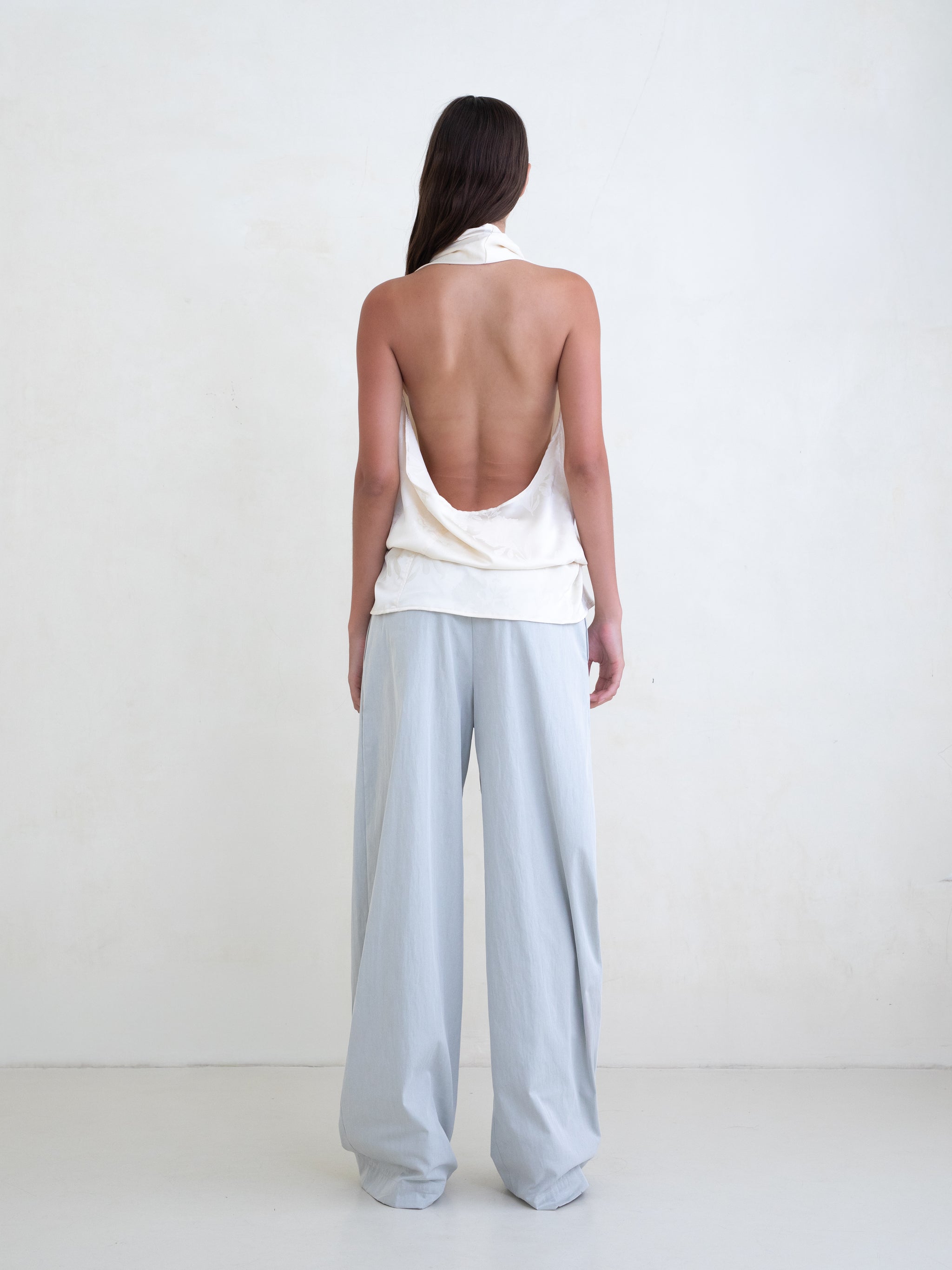 Woman wearing an off-white sleeveless halter top and light blue wide leg pants on a white background. 