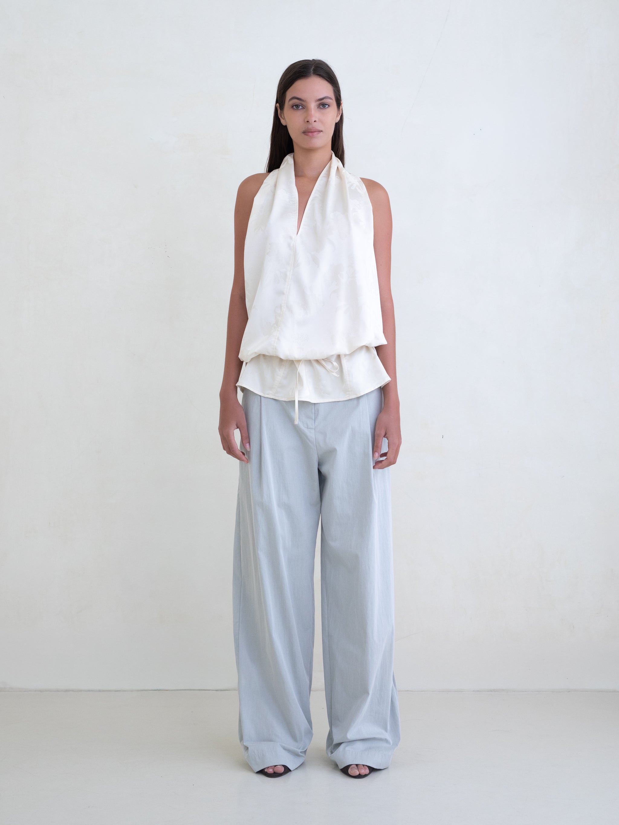 Woman wearing an off-white sleeveless halter top and light blue wide leg pants on a white background. 