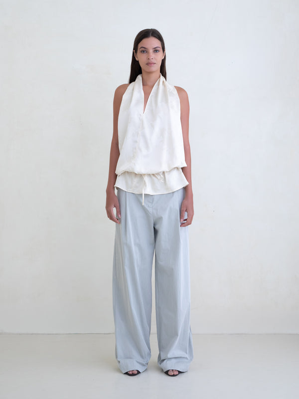 Woman wearing an off-white sleeveless halter top and light blue wide leg pants on a white background. 