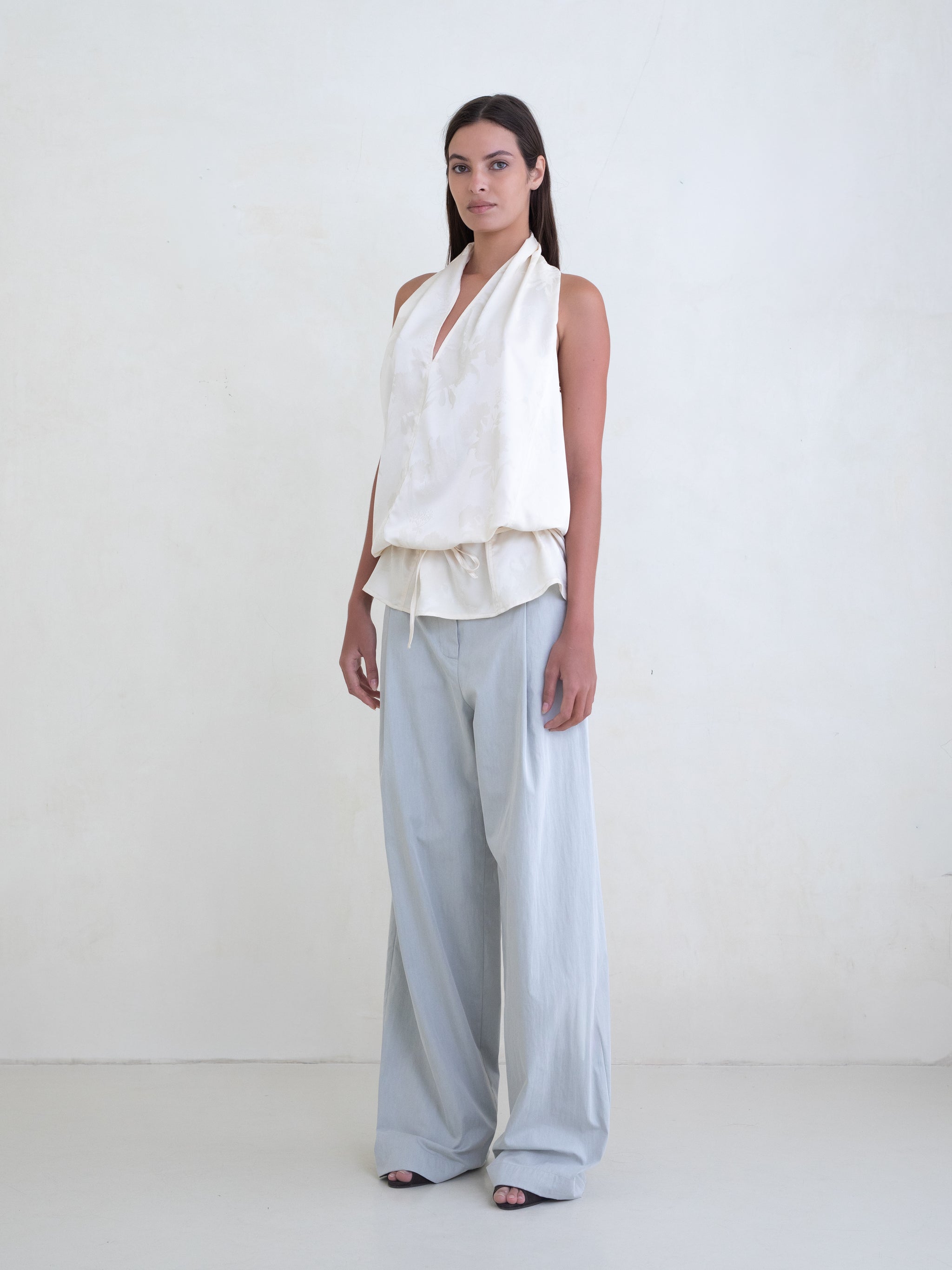 Woman wearing an off-white sleeveless halter top and light blue wide leg pants on a white background. 