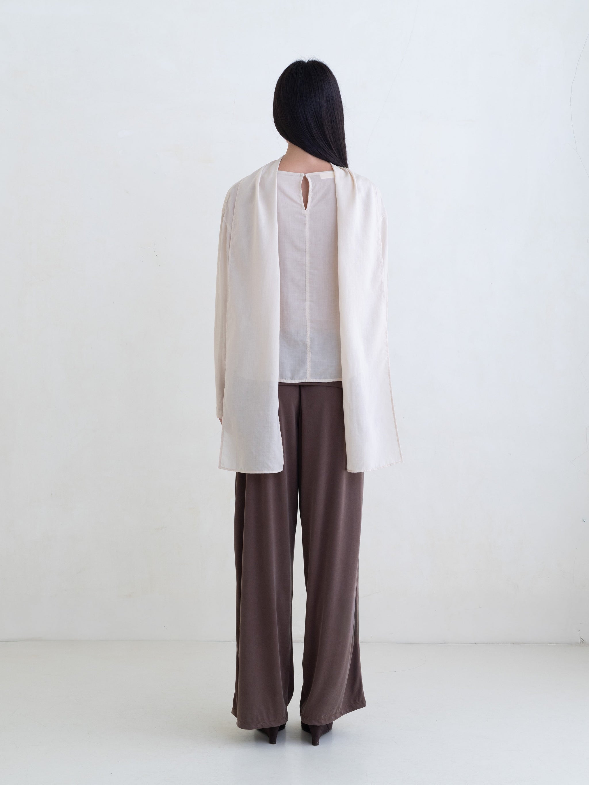 Woman wearing a cream long sleeve blouse and brown pants on a white background. 