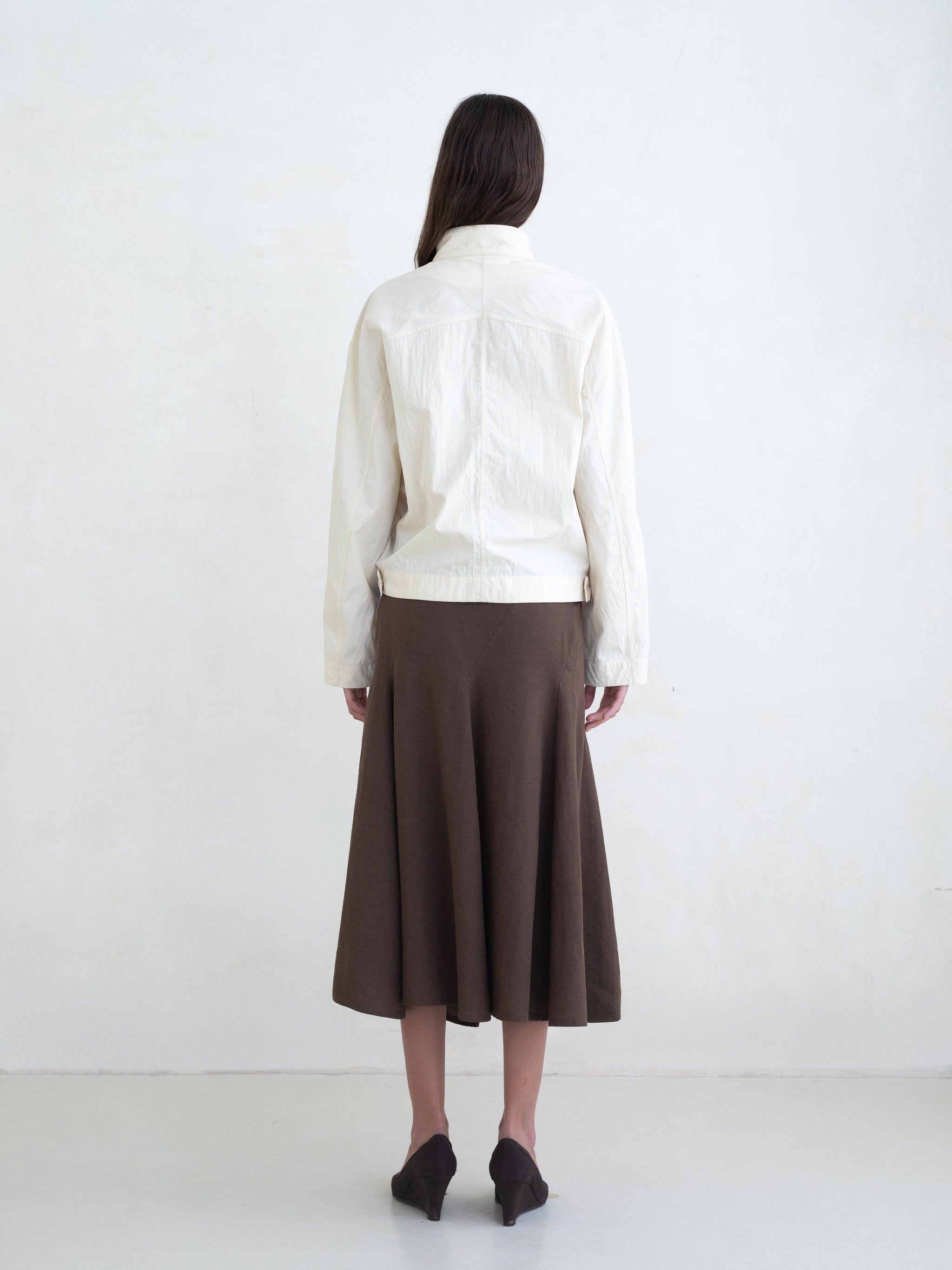 Woman wearing a cream asymmetric jacket and a brown midi skirt on a white background.