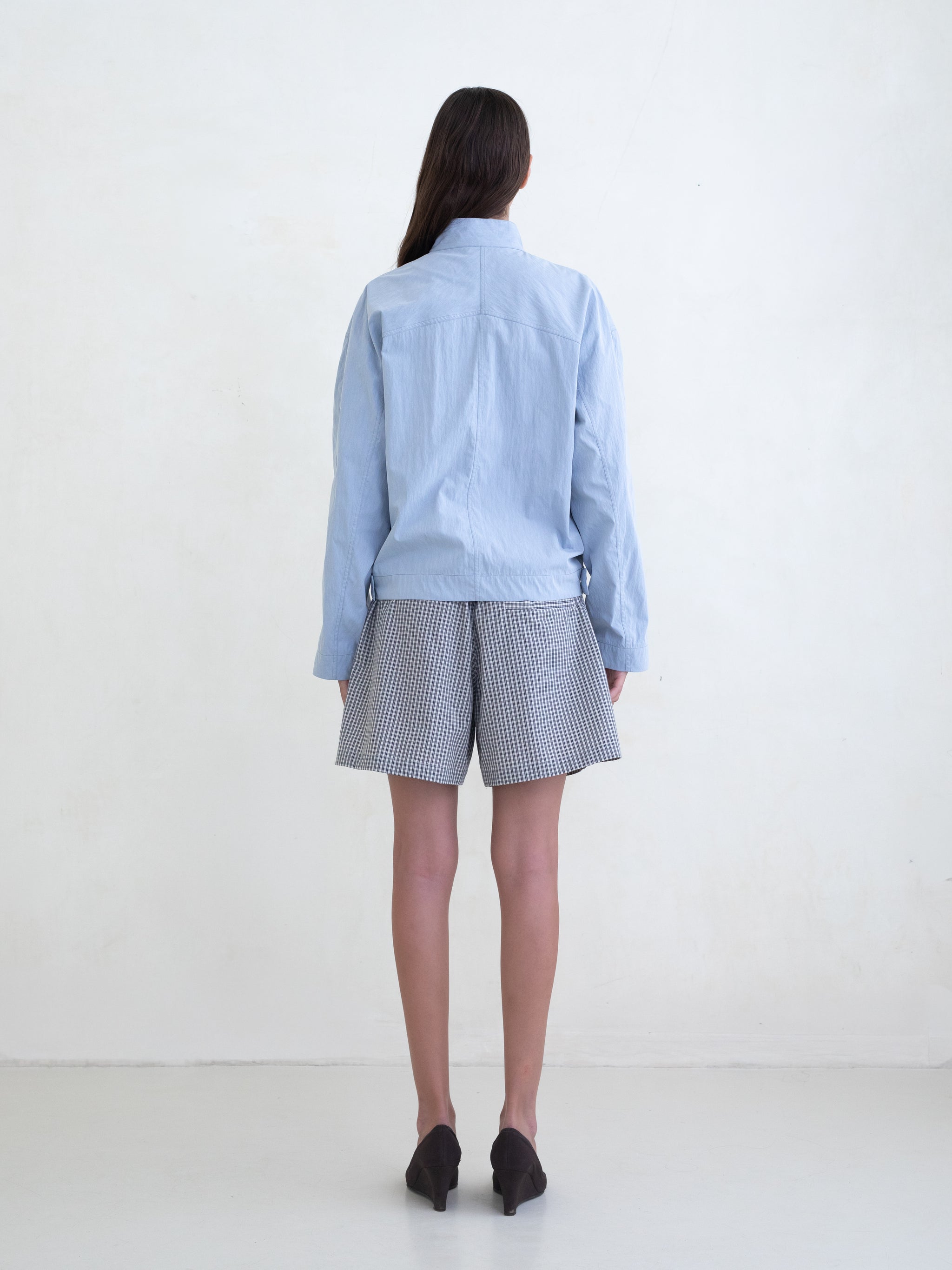 Woman wearing a light blue asymmetric jacket and a black plaid boxer shorts on a white background. 