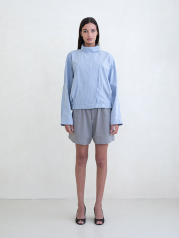 Woman wearing a light blue asymmetric jacket and a black plaid boxer shorts on a white background. 