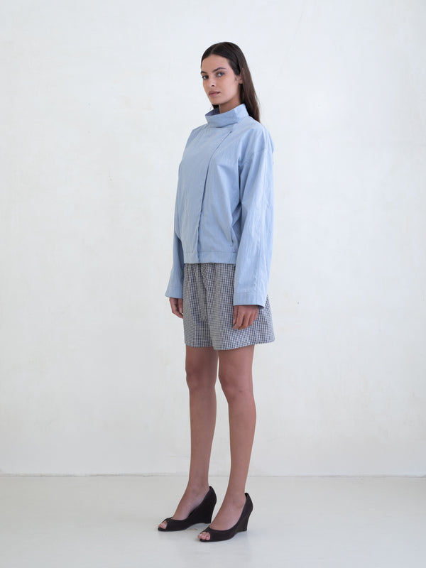 Woman wearing a light blue asymmetric jacket and a black plaid boxer shorts on a white background. 