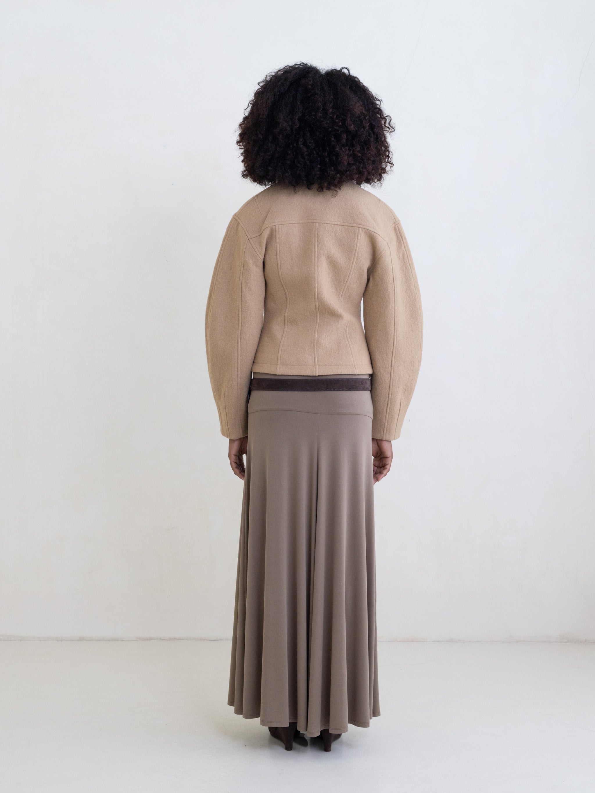 Woman wearing a beige zip-front jacket and a taupe maxi skirt on a white background. 