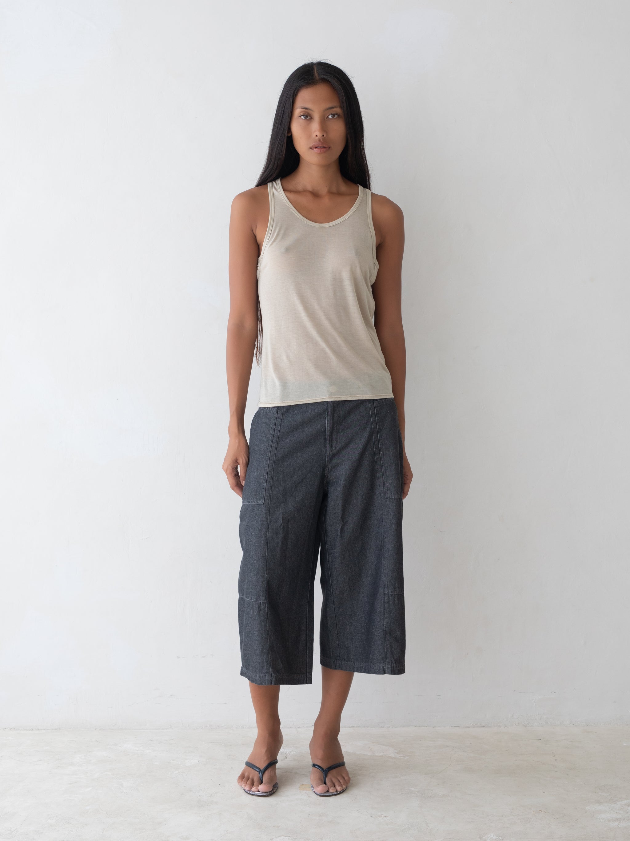 Woman wearing a beige tank top and dark gray pants on a white background