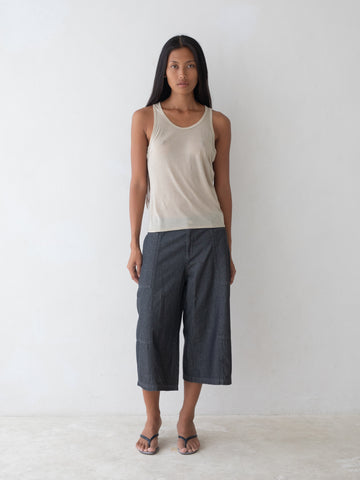 Woman wearing a beige tank top and dark gray pants on a white background