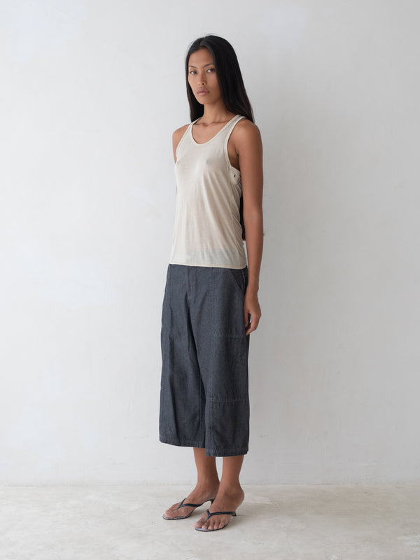 Woman wearing a beige tank top and dark gray pants on a white background